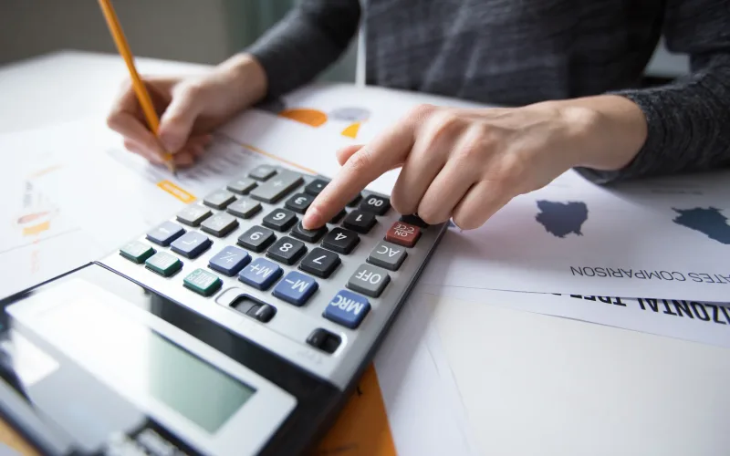 Close-up of female hand counting with calculator, papers all around on table. Businesswoman working with documents