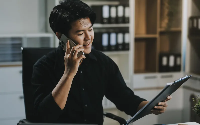 Happy smiling businessman wearing casual clothes and using modern smartphone in his home office during the day, typing, touching the screen, browsing the internet or writing text messages.