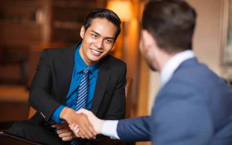 Closeup of two smiling business men shaking hands in cafe. One man is sitting back to camera.